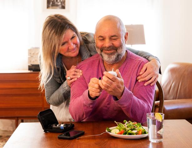 A diabetic patient checking his blood sugar at home with the support of his wife. 