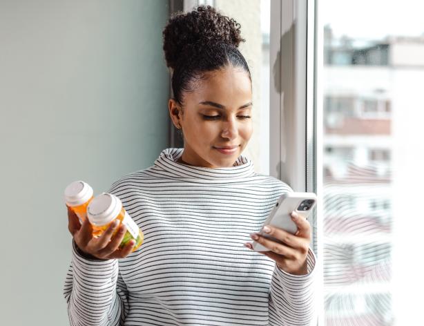 Content woman holding two prescription pill bottles and looking at her phone